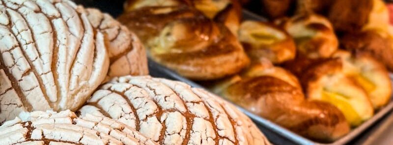 Freshly baked conchas and other pastries on trays in a Mexican bakery.